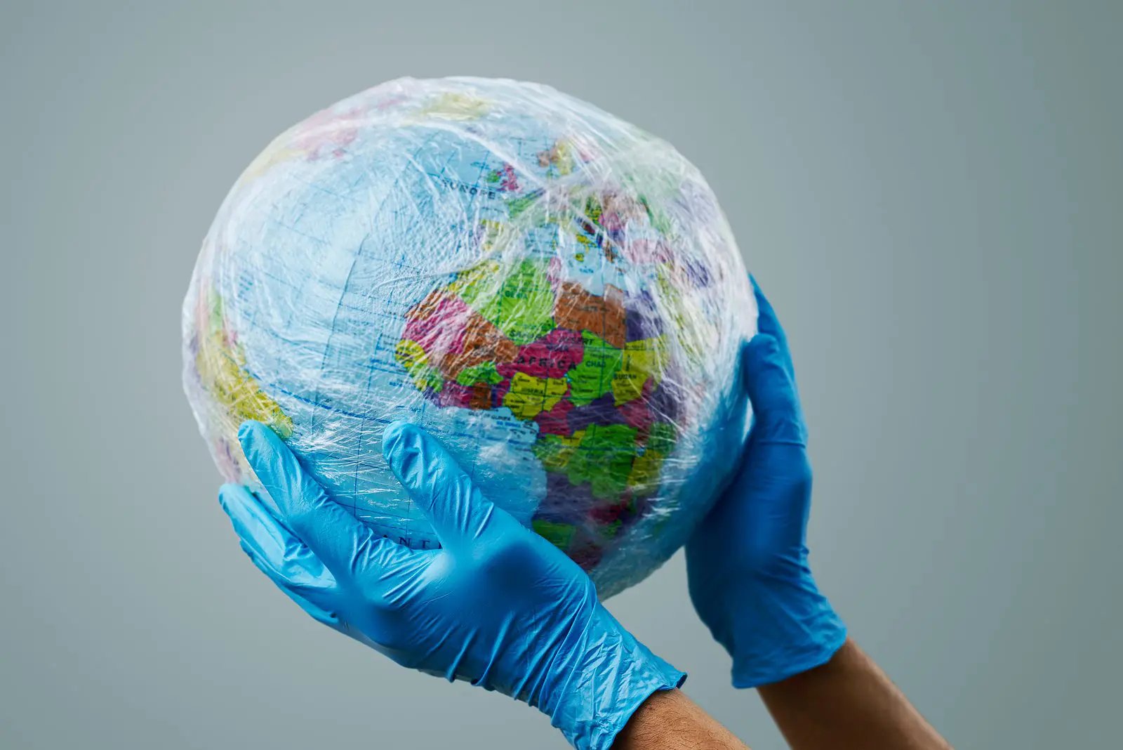 a doctor man wearing blue surgical gloves holding a world globe wrapped in plastic, depicting the plastic contamination or the protection against the epidemic infectious diseases or the air pollution