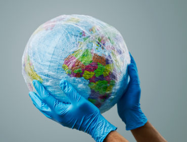 a doctor man wearing blue surgical gloves holding a world globe wrapped in plastic, depicting the plastic contamination or the protection against the epidemic infectious diseases or the air pollution